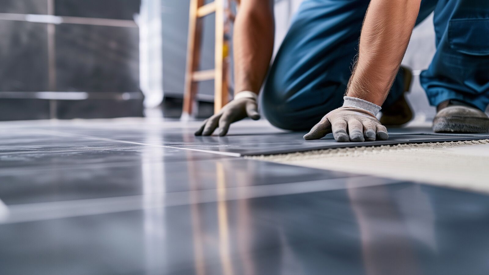 Handwerker verlegt schwarze Fliesen auf einem Boden.